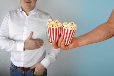 Beyaz gömlekli adam kalp bölgesinde göğsüne tutunuyor, elinde patlamış mısırla iki bardak tutuyor, problem ve eğlence kavramı, kopyalama alanı