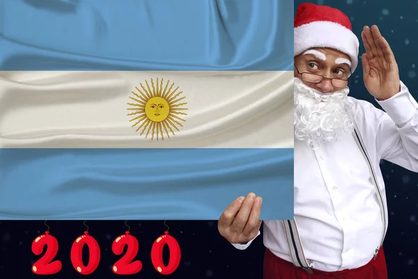 Santa Claus con barba sostiene una hermosa bandera nacional de color del estado de Argentina sobre tela, concepto de turismo, Año Nuevo y Navidad, perspectivas económicas y políticas — Foto de Stock