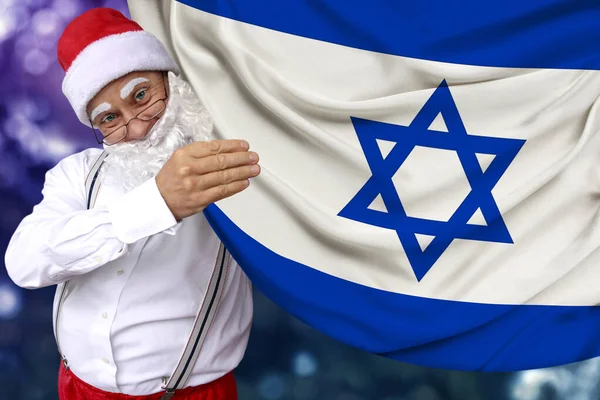 Santa Claus met een baard houdt de prachtige gekleurde nationale vlag van de staat Israël op stof, concept van toerisme, Nieuwjaar en Kerstmis, economische en politieke vooruitzichten — Stockfoto