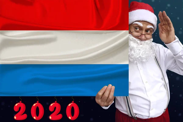Père Noël avec une barbe tient le beau drapeau national coloré de l'État du Luxembourg sur le tissu, concept de tourisme, Nouvel An et Noël, perspectives économiques et politiques — Photo