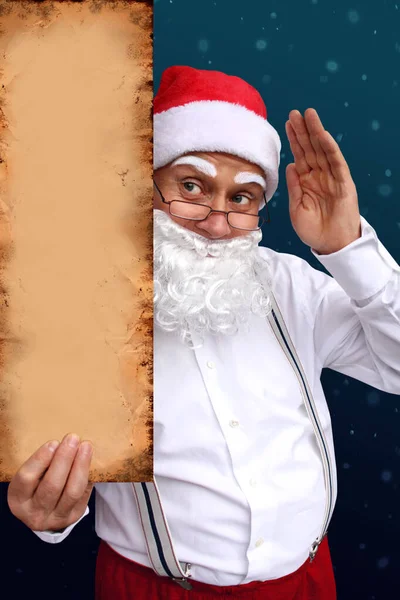 Papai Noel com barba segura um belo cartaz em branco, em branco, velho papel, papelão, em branco para o designer, padrão para anúncios, convites, saudações, vertical, mock up, close-up, espaço de cópia — Fotografia de Stock