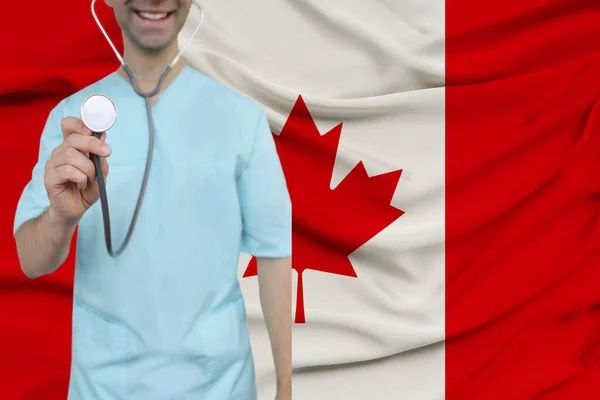 Mannelijke arts in uniform professionele kleding met een stethoscoop staat tegen de achtergrond van de nationale vlag, het concept van de gezondheidszorg en ziektekostenverzekering van het land, close-up, kopieerruimte — Stockfoto