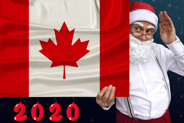 Santa Claus with a beard holds a beautiful photo of the colored national flag of the modern state of Canada with a festive date for 2020, the concept of tourism, the new year, economic prospects — Stock Photo, Image