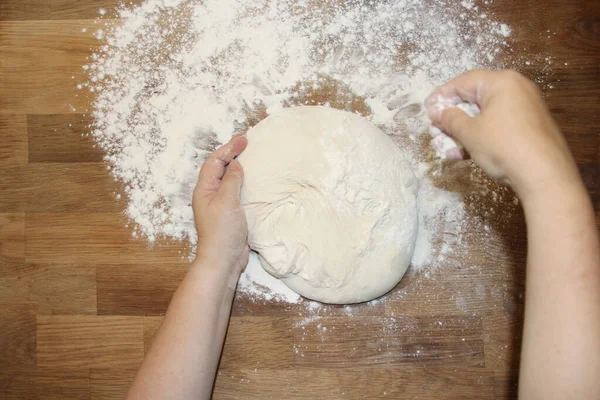 Female hands knead the dough on a wooden table, sprinkled with flour, close-up, selective focus, home cooking concept, copy space — Stock Photo, Image