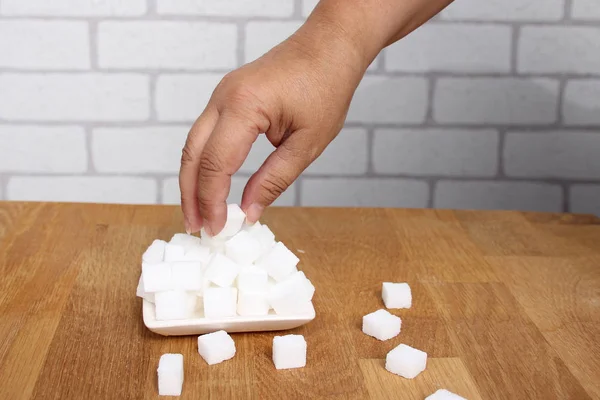 Main féminine prend du sucre raffiné dans un bol à sucre en morceaux sur une table en bois, concept de consommation excessive de sucre, diabétique, gros plan, espace de copie — Photo