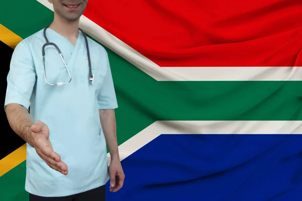Medico di sesso maschile in uniforme abiti professionali con uno stetoscopio accoglie i pazienti con la mano sullo sfondo della bandiera nazionale, il concetto di assicurazione sanitaria e medica del paese — Foto Stock