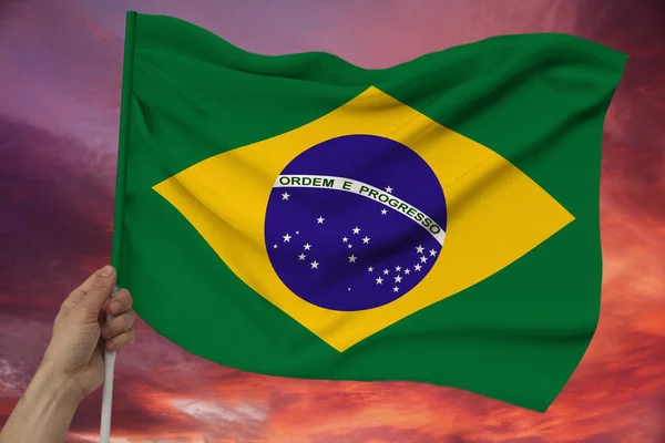 Mannelijke hand houdt Brazilië nationale vlag op Sky achtergrond met wolken op luxe satijn textuur, zijde met golven, close-up, kopie ruimte, concept van reizen, economie, politiek — Stockfoto