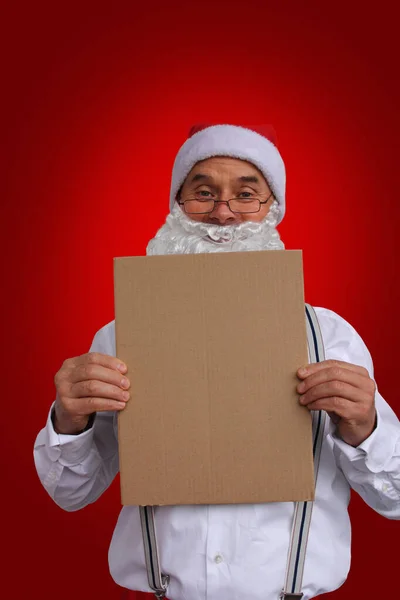 Papai Noel em óculos, em uma camisa branca com suspensórios, segura uma folha de papelão em suas mãos, forma em branco, mock up, conceito de Natal, close-up — Fotografia de Stock