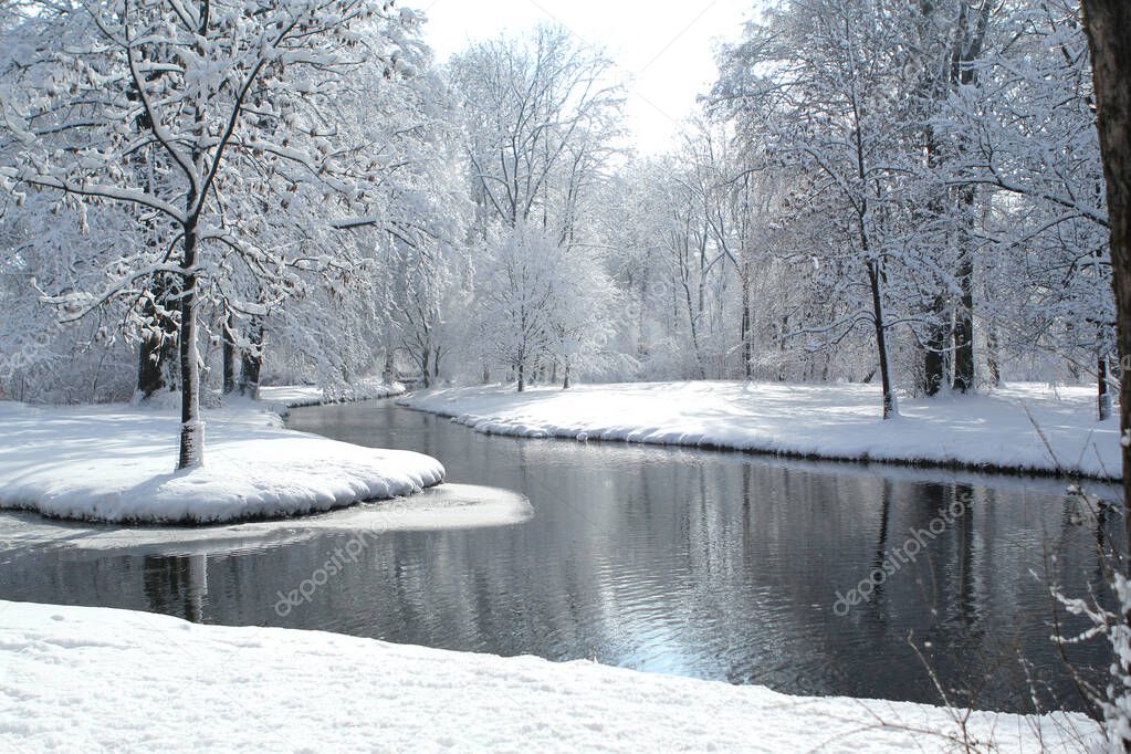 beautiful winter landscape with snowy trees in a park by a winding Isar river in Munich
