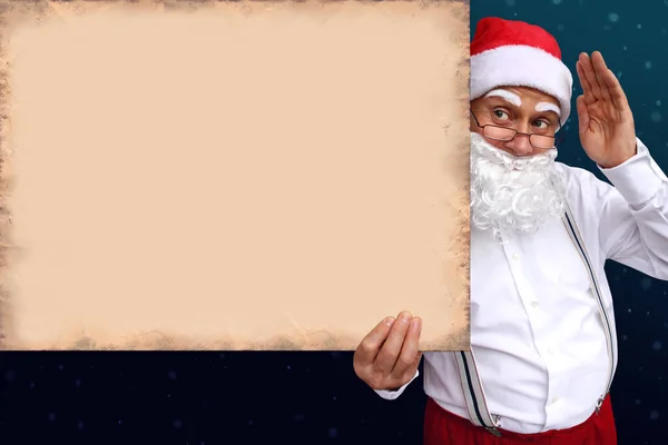 Santa Claus con barba sostiene un hermoso cartel en blanco, en blanco, de papel viejo, cartón, en blanco para el diseñador, patrón para anuncios, invitaciones, saludos, calendario, maqueta, primer plano, espacio de copia — Foto de Stock