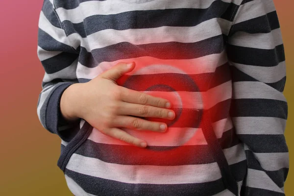 Niño, niño en un jersey a rayas sostiene su estómago por la mano, círculos rojos de dolor pulsátil, concepto de dolencia — Foto de Stock