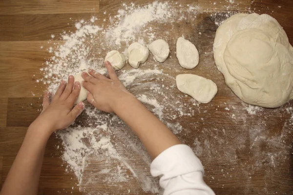 Child sculpts flour products from dough on a wooden table, sprinkled with flour, close-up, selective focus, home cooking concept, copy space — Stockfoto