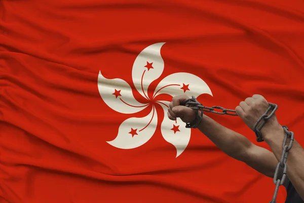 Male coarse hands chained in heavy iron chains against the backdrop of the Hong Kong national flag, crime concept in the country, arrest, lawlessness, repression, close-up, copy space — Stock Photo, Image