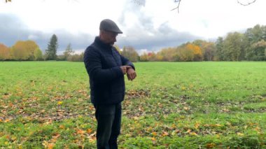 Orta yaşlı bir adam saatine hevesle bakıyor, sonbahar parkında kadınını bekliyor, heteroseksüel ilişkiler kavramı, yakın çekim.