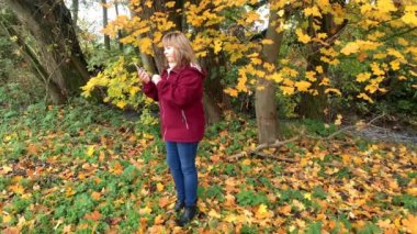 Sonbahar parkında kot pantolon ve bordo ceketli orta yaşlı bir kadın telefonda duygusal olarak konuşuyor, iletişim konsepti, yakın plan.