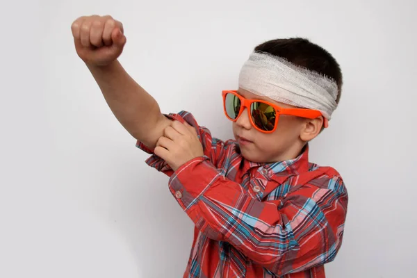 Junge mit dunkler Sonnenbrille, kariertes Hemd, den Kopf bandagiert, prüft seine Muskeln, das Konzept der Geduld der Kinder, Nahaufnahme — Stockfoto