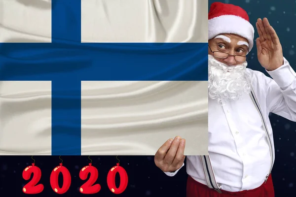 Santa Claus con barba sostiene una hermosa bandera nacional de color del estado de Finlandia sobre tela, concepto de turismo, Año Nuevo y Navidad, perspectivas económicas y políticas —  Fotos de Stock