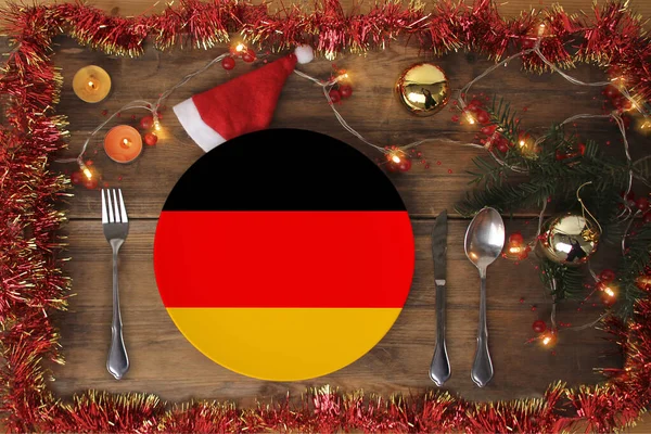 Wunderschöne weihnachtliche Komposition mit einem Teller mit der Nationalflagge Deutschlands, serviert mit Besteck, Lametta, Girlanden, Fichtenzweig, Kerzen, dem Konzept des traditionellen Weihnachtsessens, gastronomisch zu — Stockfoto