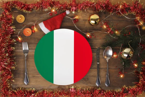 Mooie kerstcompositie met een bord met de nationale vlag van Italië, kerstversiering, bloemenslingers, kaarsen, het concept van traditioneel nieuwjaarseten, gastronomisch toerisme — Stockfoto
