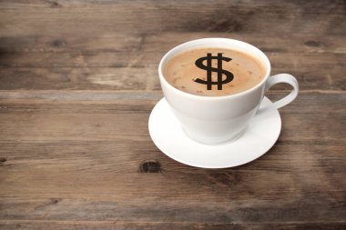 Beyaz bardakta kapuçino kahvesi ve tabakta bir dolar işareti, eski ahşap bir masada fotokopi alanı, pahalı kahve konsepti.