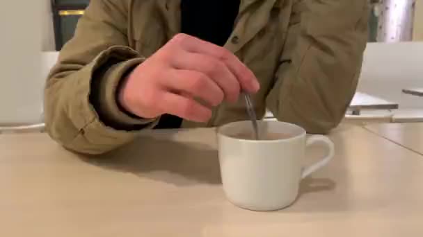 男人在咖啡店里用勺子搅拌咖啡中的糖 用一个白色杯子里的勺子 — 图库视频影像