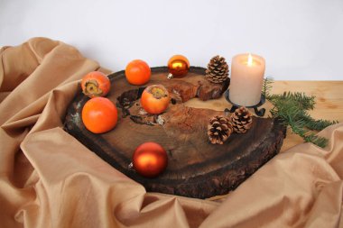 Eski bir ağaç kesimindeki güzel kompozisyon, ipek kumaştan yapılmış kumaşlar, yanan bir mum, koniler, turuncu Noel topları ve hurma ağaçları, Noel konsepti.