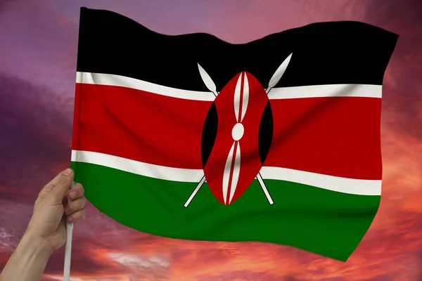 Mano maschile tiene sullo sfondo del cielo con le nuvole la bandiera colorata del Kenya su una lussuosa texture di raso, seta con onde, primo piano, spazio copia — Foto Stock