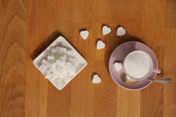 Sucre en vrac dans une tasse à thé rose et une soucoupe, tranches raffinées, pinces à sucre, bonbons en forme de coeur, concept de consommation excessive de sucre, diabétique, gros plan, espace de copie, vue de dessus — Photo