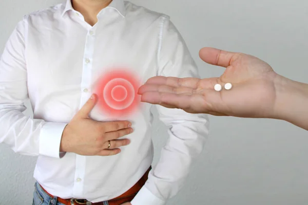 Mujer, médico, enfermera, sostiene píldoras de palma blanca a un hombre en una camisa con un círculo rojo, un símbolo de dolor pulsátil que se aferra al pecho en el corazón, concepto médico — Foto de Stock