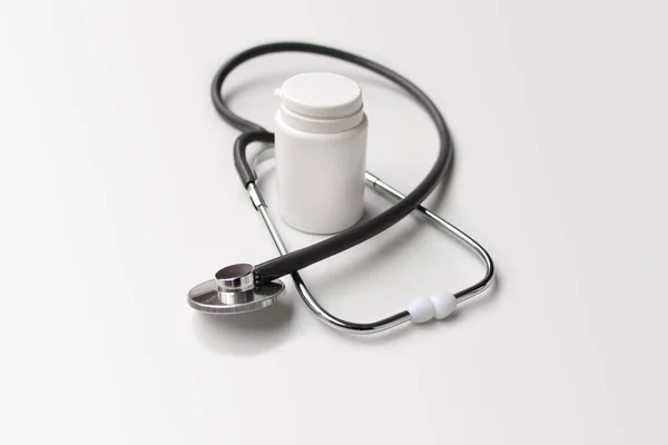 Estetoscópio médico encontra-se em um fundo branco em torno de uma lata de medicina branca vazia, forma para um designer, close-up, espaço de cópia — Fotografia de Stock
