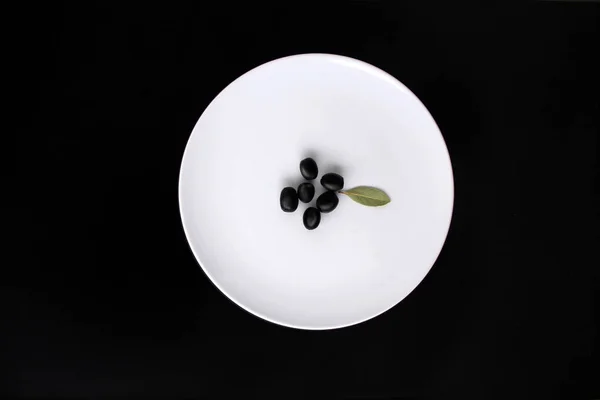 Aceitunas negras con agujeros, sin hueso, se encuentran en un plato blanco, fondo negro con gotas, espacio para copiar — Foto de Stock