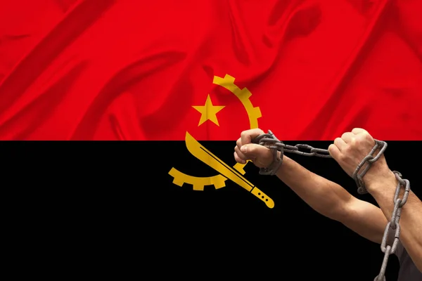 Male hands of a prisoner in iron chains against the background of the national flag of Angola on beautiful silk, concept of political repression, crime, imprisonment, violation of rights and freedoms — Stock Photo, Image