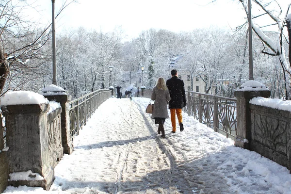 Man and woman walk along the bridge together among the cold white landscape of the city of Munich in the snow, a park in winter, the concept of love, a happy marriage — Stock Photo, Image