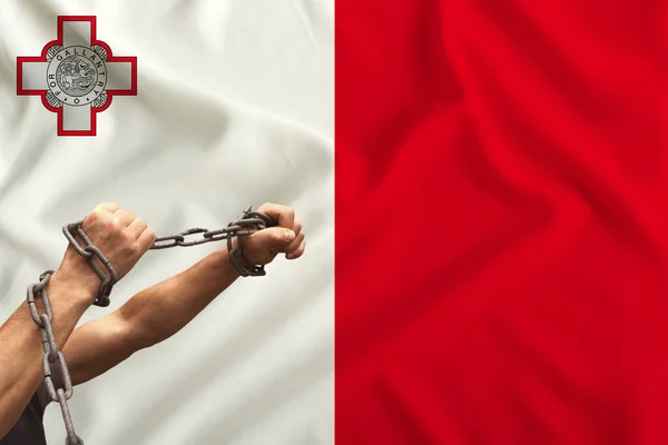 male hands of a prisoner in iron chains against the background of the national flag of Malta on silk fabric, the concept of political repression, crime, imprisonment, violation of the rights, freedoms