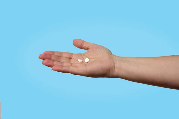 Mujer extiende su mano con dos píldoras blancas sobre un fondo azul, concepto de seguro de salud, atención médica, asistencia, aislamiento, espacio de copia — Foto de Stock