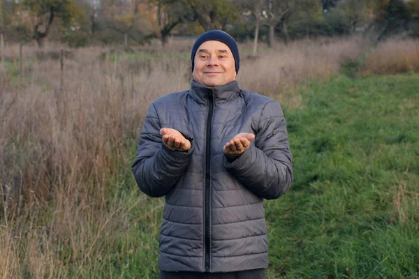 Velho homem positivo em um chapéu com um sorriso mantém as mãos na frente dele na natureza, o conceito de um estilo de vida saudável e unidade com a natureza, close-up — Fotografia de Stock