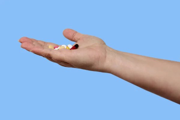 Female hand holds out, offering, a handful of colored pills and capsules, close-up, color background, copy space, concept of medical care, treatment — Stock Photo, Image