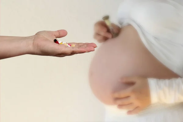 female hand holds out, offering, a handful of colored pills and capsules, close-up, blurred image of a pregnant woman in the background, copy space, concept of pregnancy complications, treatment