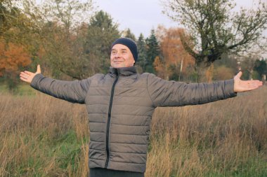 Gülümseyen, şapkalı yaşlı, pozitif bir adam kollarını açık havada açtı. Sağlıklı yaşam tarzı ve doğayla bütünlük kavramı, yakın plan.