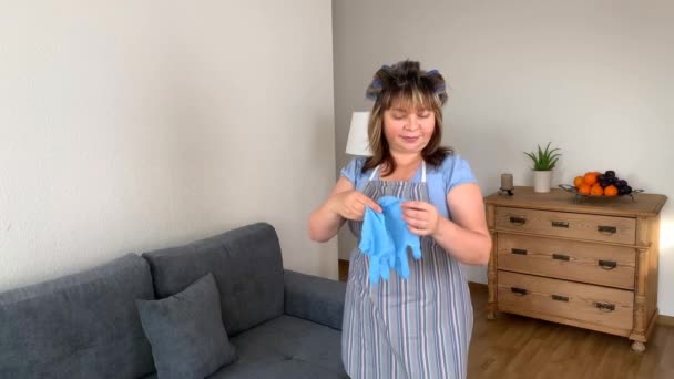 Középkorú Vicces Háziasszony Kötényben Hajcsavaróval Védőkesztyűt Vesz Fel Ház Tisztítására — Stock videók