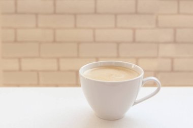 Beyaz bir masada beyaz bir kahve, beyaz bir kapuçino, beyaz bir tuğla duvarın arka planı, yan görünüş, boşluk tasarrufu.