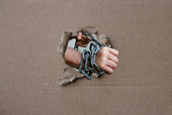 male hands wrapped in a thick heavy iron chain, a symbol of the arrest of a criminal