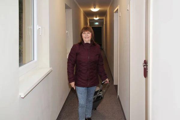 Foto horizontal de una mujer, un turista, caminando a lo largo de un largo pasillo del hotel con una maleta más allá de la puerta, concepto turístico —  Fotos de Stock