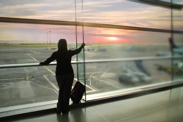 女乘客等着他的航班，站在窗前看着机场跑道，一场旅行音乐会 — 图库照片