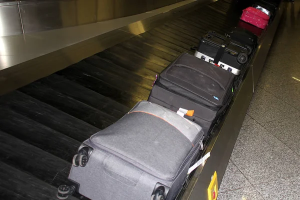 Muitas malas de diferentes cores na sala de chegada dos passageiros do aeroporto jazem no cinto de bagagem uma após a outra, o conceito de receber ou perder bagagem — Fotografia de Stock