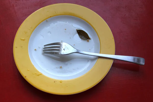 Plato usado amarillo vacío con tenedor, pan rallado y una pequeña hoja de laurel — Foto de Stock