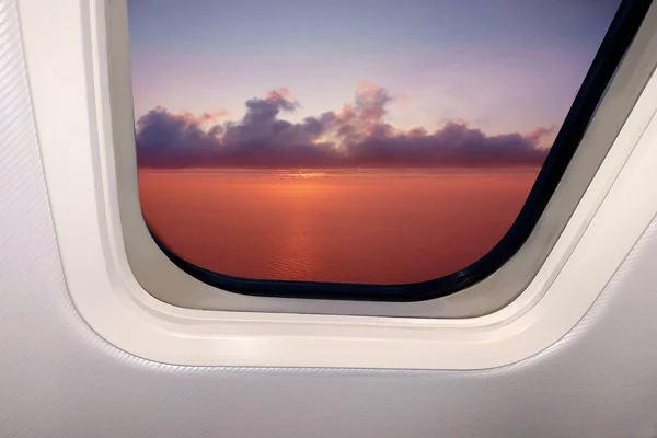 Hermoso cielo paisaje de puesta de sol roja con nubes y el mar por debajo a través de la portilla de un avión, concepto de viaje — Foto de Stock