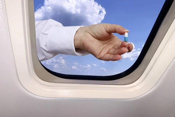Vrouwelijke hand met pillen op de achtergrond van een prachtig hemels landschap van blauwe lucht met pluizige wolken achter de patrijspoort van een vliegtuig, reisconcept — Stockfoto
