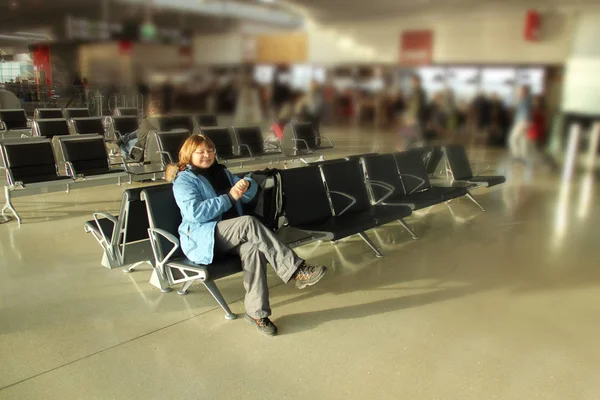 Pasajera esperando su vuelo sentado en un sillón en el salón del aeropuerto, concierto de viaje —  Fotos de Stock
