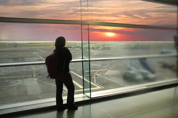 Passageira, esperando por seu voo, fica na janela e olha para a pista do aeroporto, um concerto de viagem — Fotografia de Stock